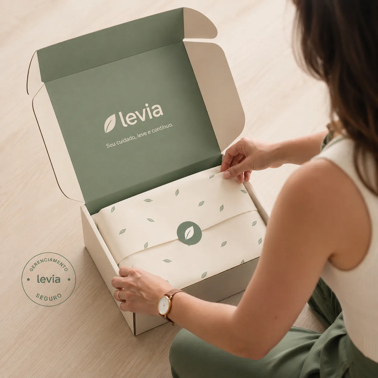 Pessoa abrindo uma embalagem da Levia sobre uma mesa clara, com o selo de gerenciamento seguro visível.