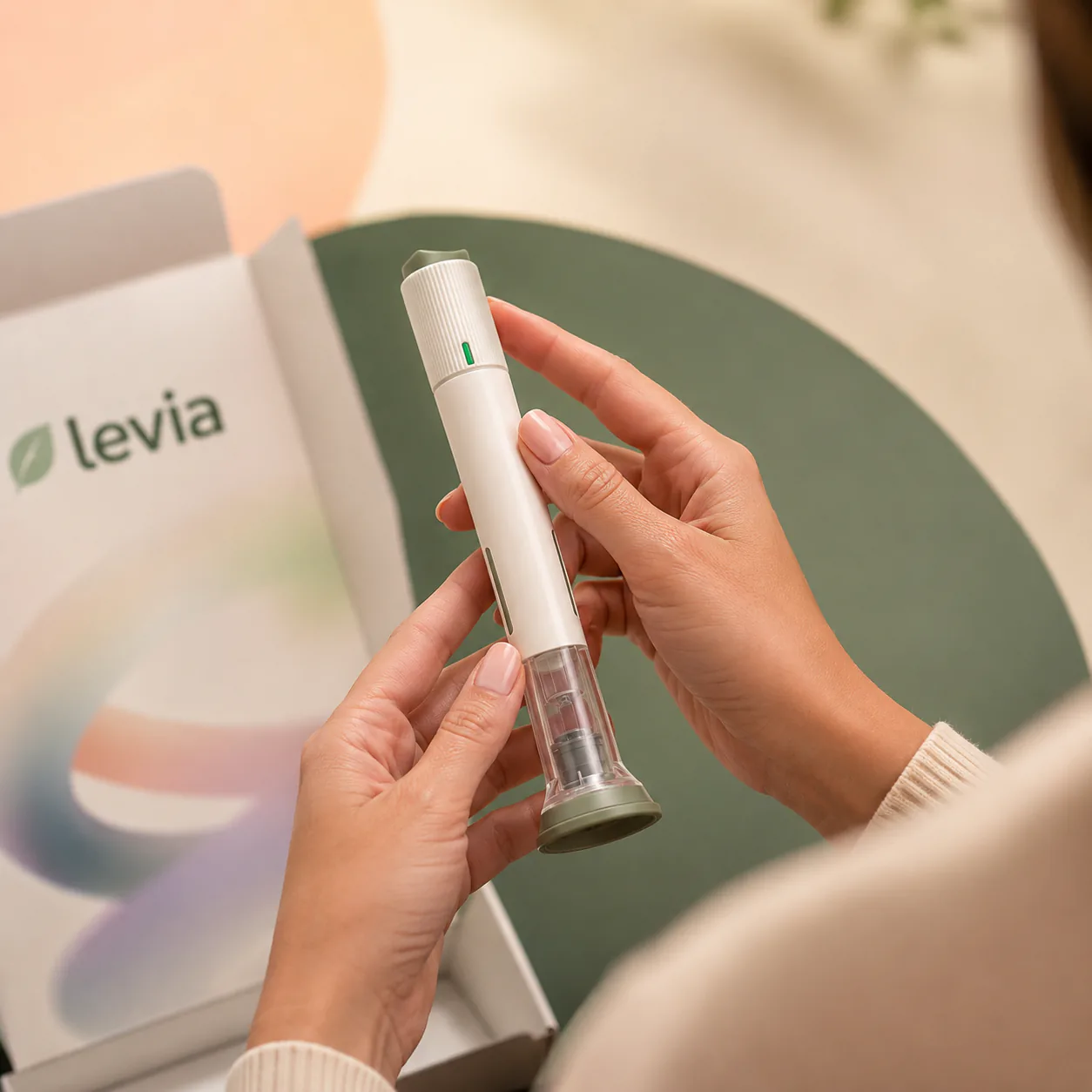 Mãos segurando uma caneta injetável junto a uma embalagem da Levia.
